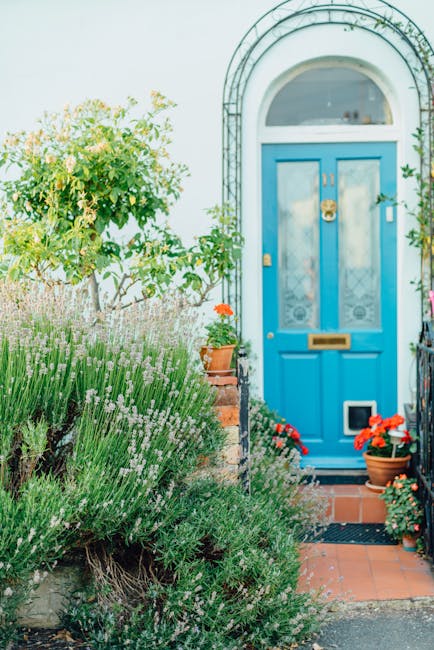 A close-up view of the exterior of a red brick house showing a small front garden area with neatly trimmed low brick wall. The house features white-framed sash windows on the ground floor, some with c